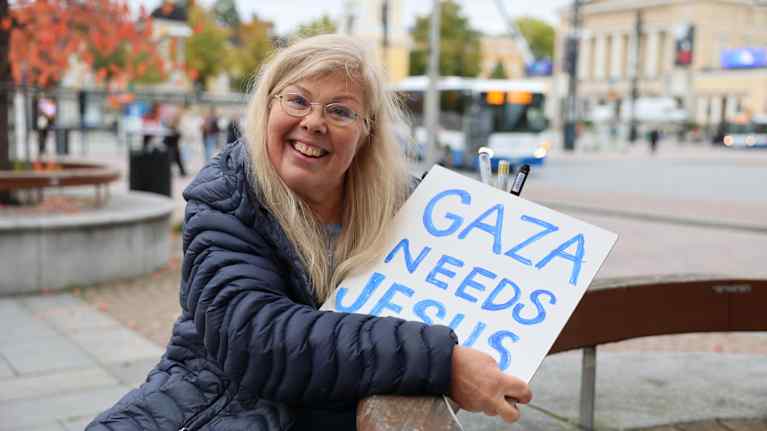Hymyilevä nainen pitelee kylttiä, jossa teksti Gaza needs Jesus.