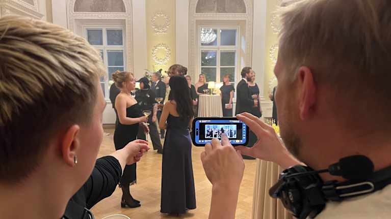 Suden kyyneleet -elokuvan kuvauksissa avustajia astelellaan oikeisiin paikkoihin kännykästä näkyvän kuvan avulla.