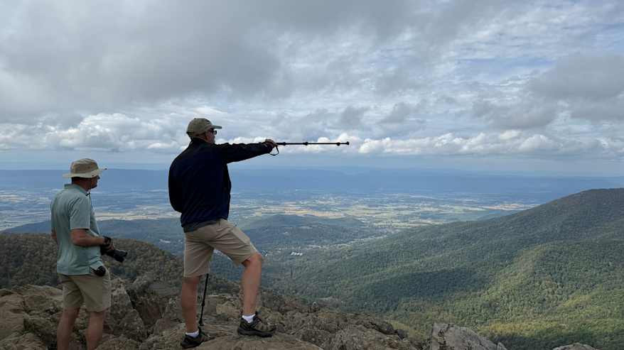 Mies seisoo vuoren huipulla nauttien vaikuttavasta maisemasta.