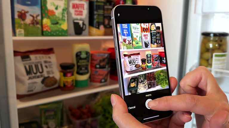 Henkilö kuvaa jääkaapin sisältöä, jossa on monenlaisia elintarvikkeita.