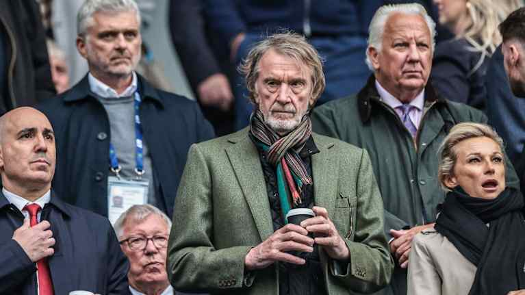 Mies seuraa jalkapallo-ottelua kahvikuppi kädessään.