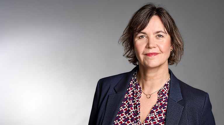 Henkilö on pukeutunut  tummansiniseen bleiseriin ja kuvioituun kauluspaitaan.