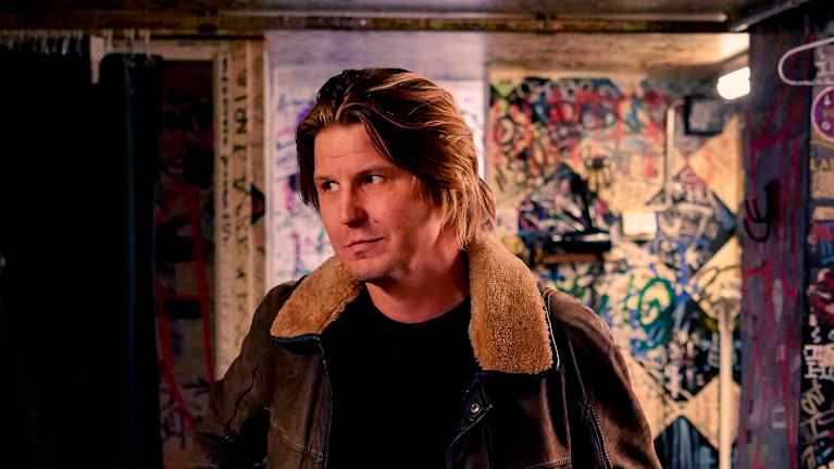 Markus Krunegård Tavastian takahuoneessa. Seisoo ja katsoo sivulle kädet takin taskuissaan.