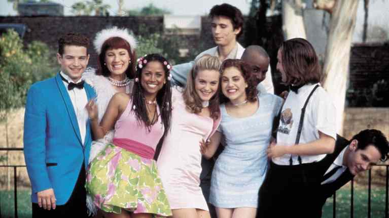 Ryhmä Clueless-elokuvan nuoria näyttelijöitä pukeutuneina värikkäisiin juhlavaatteisiin ulkona iloisessa tunnelmassa.