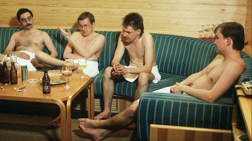 Neljä henkilöä istuu pyyhkeet ympärillään saunan takkahuoneessa.