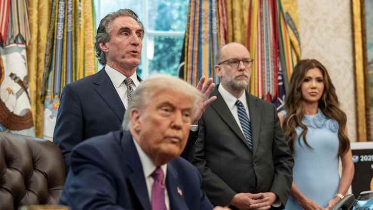 Trump happaman näköisenä istuu etualalla, taustalla seisoo mm. Russell Vought.