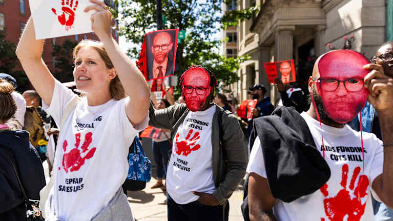 Mieleosoittajat vastustavat Russel Voughtia, osalla naamari, jossa hänen kuvansa.