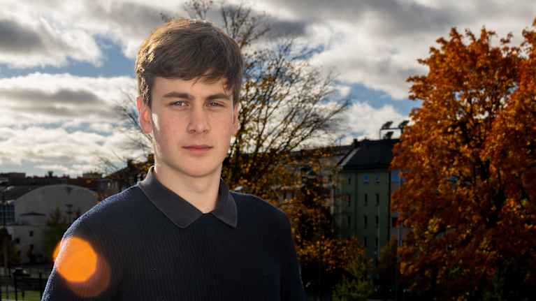 Tuukka Taponen katsoo kameraan. Kuvattu ulkona, oranssi vaahtera taustalla.