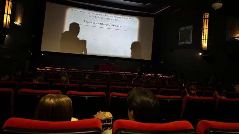 Kaksi ihmistä popcornien kanssa elokuvissa. Kuva kuvattu takaa päin. 