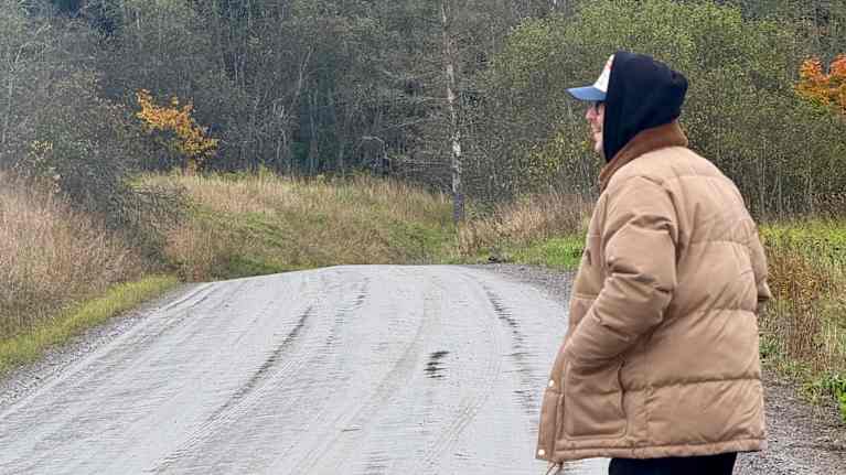 Miikka "Hätä-Miikka" Niiranen seisoo märällä hiekkatiellä. Taustalla puita ruskan väreissä.