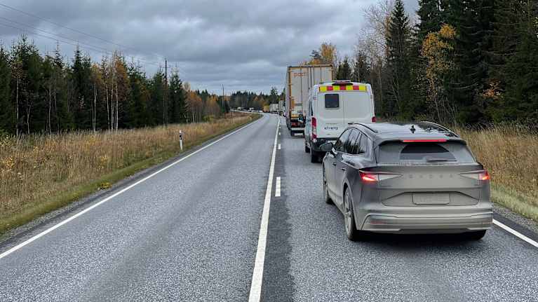 Maantiellä liikennettä harmaana ja pilvisenä syyspäivänä. Kuvassa näkyy pitkä jono autoja oikealla kaistalla. 