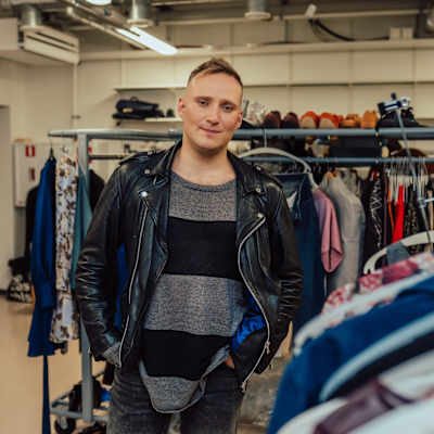 Elämäni Biisin Lauri Mikkola seisoo vaaterekin edessä pukeutuneena nahkatakkiin ja raidalliseen puseroon. Taustalla näkyy erilaisia vaatteita.