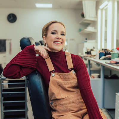 Johanna Rauma istuu rentoutuneena kampaamotuolissa, taustalla näkyy meikkitarvikkeita ja peilejä. Elämäni Biisissä.