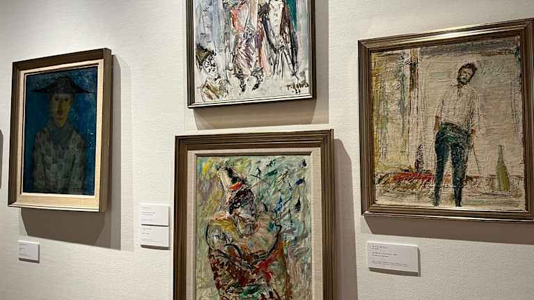 Valkoisella seinällä on neljä värikästä maalausta kehyksissä.