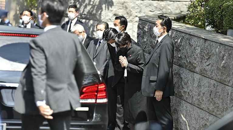 Sanae Takaichi rukoilee Shinxo Aben ruumista kuljettavan auton vierellä.