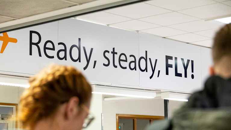 Ready, steady, Fly! -teksti seinällä lentoasemalla.