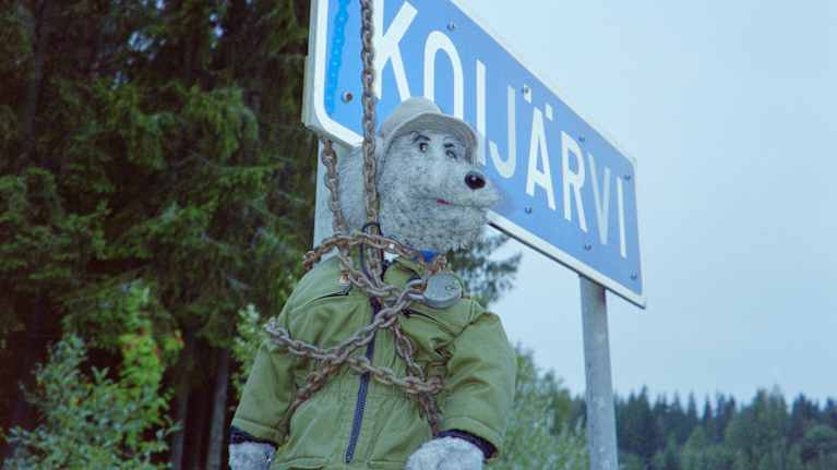 Pikku Kakkosesta tuttu käsinukkekoira Ransu Karvakuono kahliutuneena Koijärvi-tiekylttiin.