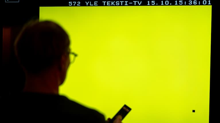 Henkilö katsoo suuresta televisiosta keltaista teksti-tv:n sivua 572.