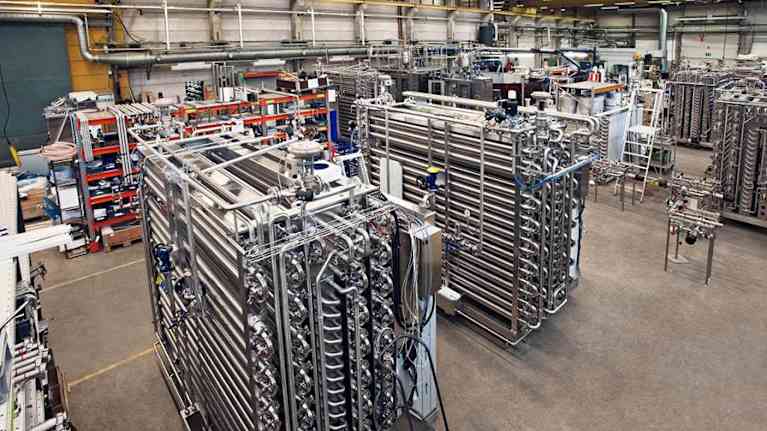 Teollisuushalli täynnä monimutkaisia putkistoja ja laitteistoja, jotka mahdollisesti liittyvät prosessiteollisuuteen tai teknologiseen tuotantoon.