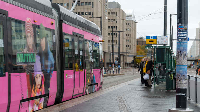 Raitiovaunu liukuu pysäkille, matkustajia odottamassa katoksen alla.