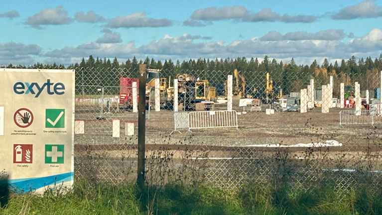 Korian datakeskuksen rakennustyömaa Kouvolassa, kuvassa perustuspilareita, työmaa-aitoja, urakoitsijan kylttejä ja kaivinkoneita.
