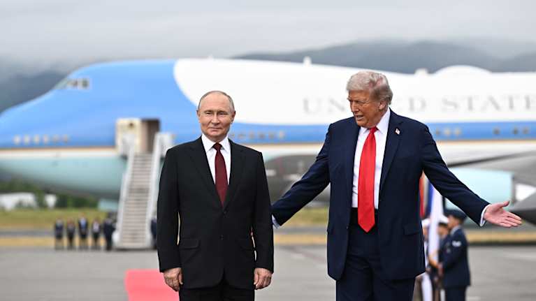 Putin ja Trump seisovat vierekkäin. Taustalla on suuri lentokone.