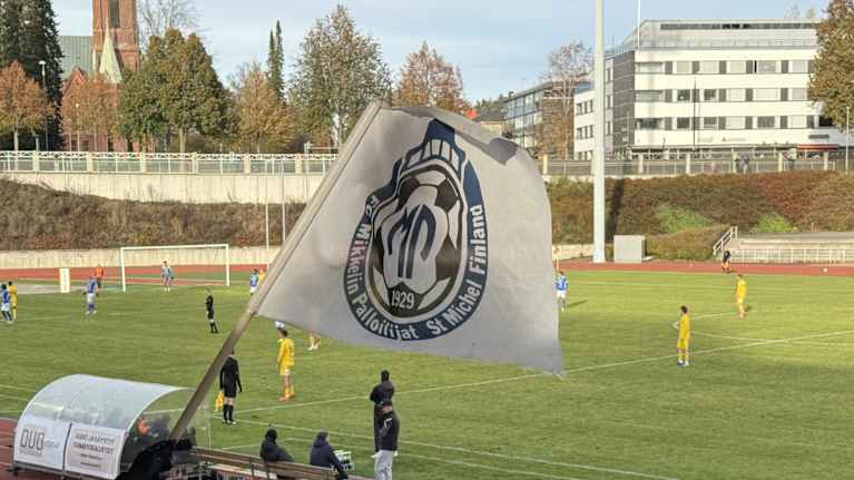 MP:n kannattajat heiluttavat seuran lippua. Taustalla Mikkelin Urheilupuistossa ottelu MP-OLS: