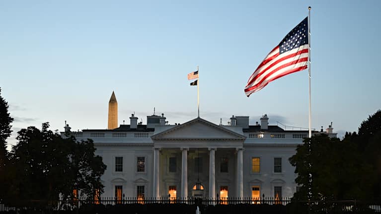 Yhdysvaltain lippu liehuu Valkoisen talon edustalla auringon nousun aikaan.