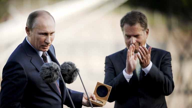 Putin puhuu mikkiin ja pitelee esinettä kädessä. Sauli Niinistö taputtaa vieressä.