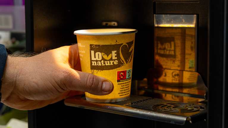 Huhtamäki Oyj:n pahvimuki kädessä kahviautomaatin luona.