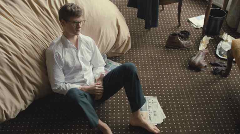 Nuori mies istuu ahdistuneen oloisena lattialla. Kuva on elokuvakohtauksesta. 