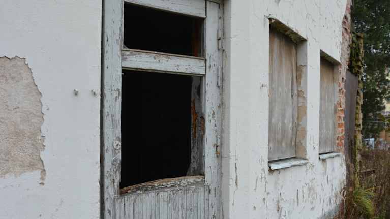 Ränsistyneen rakennuksen puinen ovi, josta puuttuu ikkuna.