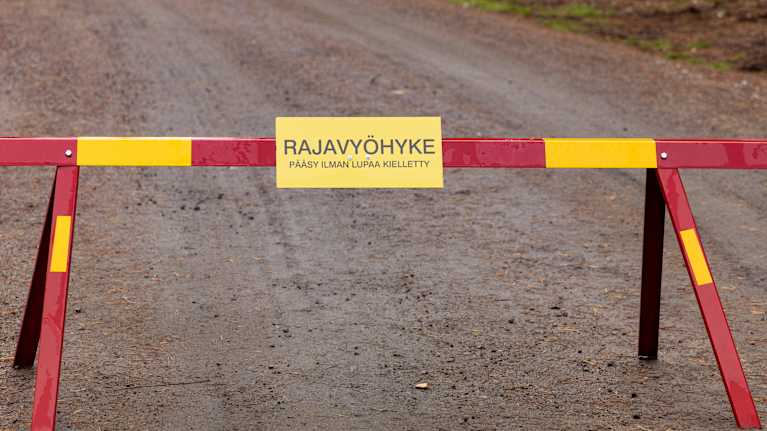 Puomi tiellä. Puomissa Rajavyöhyke, pääsy ilman lupaa kielletty -kyltti.