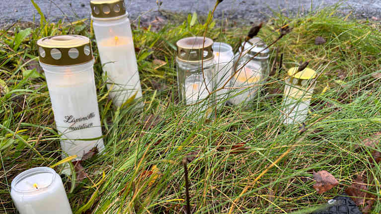 Kynttilöitä ruohikossa tien vieressä.