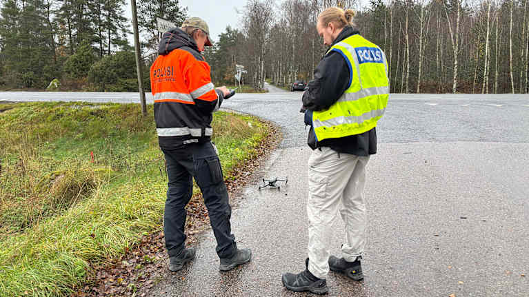 Kaksi poliisia tutkii onnettomuuspaikkaa Laitilassa. Maassa on drooni.