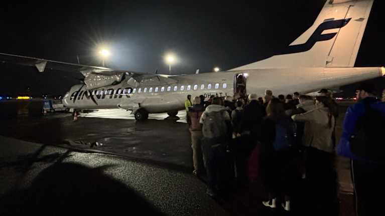 Lentomatkustajat nousemassa Finnairin potkurikoneen kyytiin pimeällä lentokentällä.