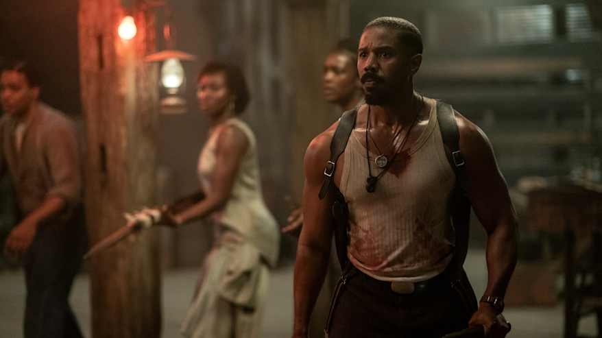 Lihaksikas musta mies pitelee aseita, päällä veren tahrima valkoinen hihaton paita.