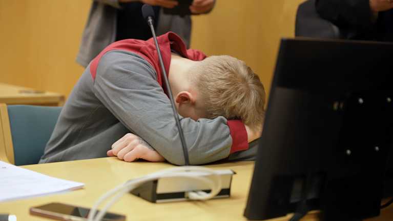 Syytetty nuorimies nojaa käsiinsä pöytää vasten oikeussalissa.