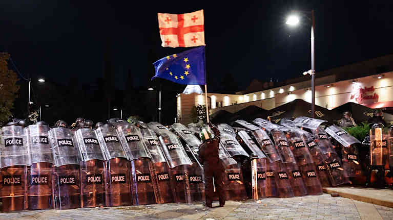 Mielenosoittaja seisoo poliisilinjan edessä Georgian ja EU:n lippujen kanssa.