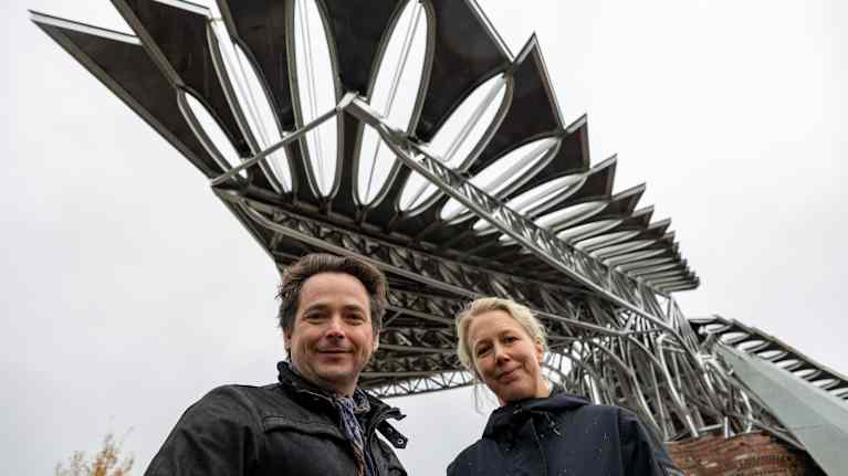 Mies ja nainen seisovat metallisen linnun levitetyn siiven alla.