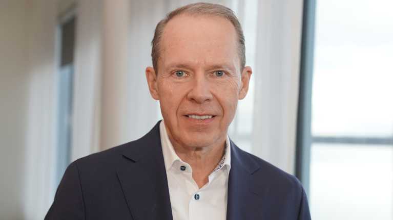 Neste, pääjohtaja Heikki Malinen seisoo pääkonttorin neuvotteluhuoneessa kameraan katsoen.