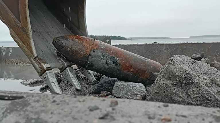 Kaivinkoneen kauha, merestä nostettu vanha, sodanaikainen lentopommi.