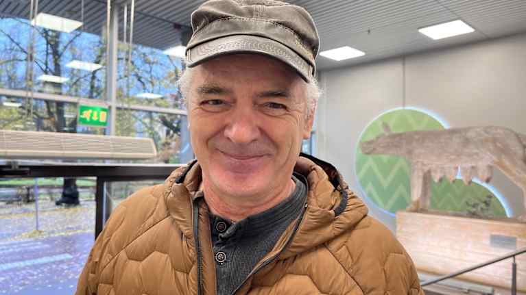 Mies talvitakissa ja lippalakissa katsoo kameraan ja hymyilee.