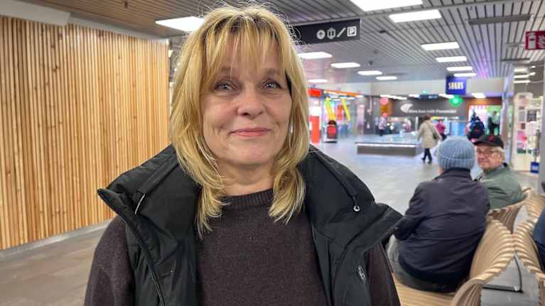 Nainen seisoo kauppakeskuksen käytävällä ja hymyilee.