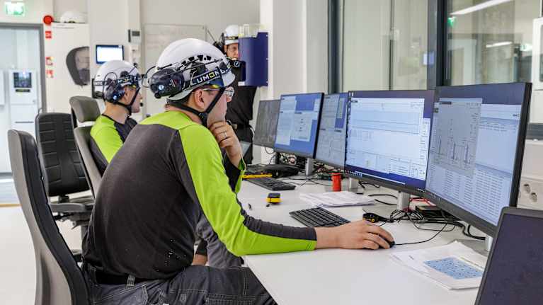 Puukuitutuotteita valmistavan koetehtaan valvomo. Kaksi miestä tarkkailee tehtaan toimintaa ja prosesseja tietokonenäytöiltä.