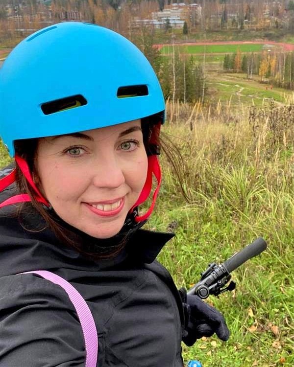 Sanna Manu hymyilee pyörän selässä. Hänellä on päässään sininen pyöräilykypärä.