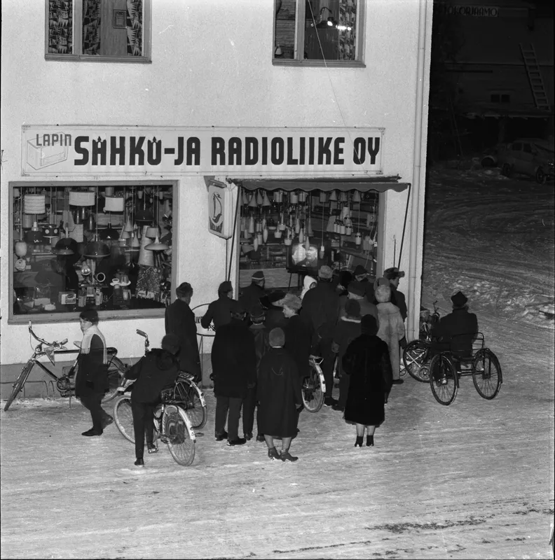 Ihmisjoukko on kerääntynyt ulos katsomaan televisiolähetystä Lapin Sähkö- ja Radioliike Oy:n näyteikkunasta, Rovakatu 13.