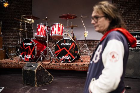 Costello Hautamäki kuvattiin tammikuussa 2024 Vapriikissa ennen Manserock-näyttelyn avaamista. Taustalla Popedan esiintymislava ja rummut.