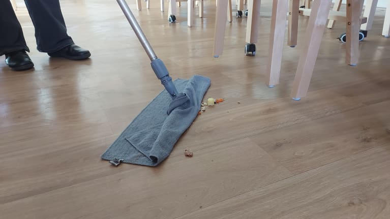 Siivooja siivoaa ruoantähteitä lattialta.
