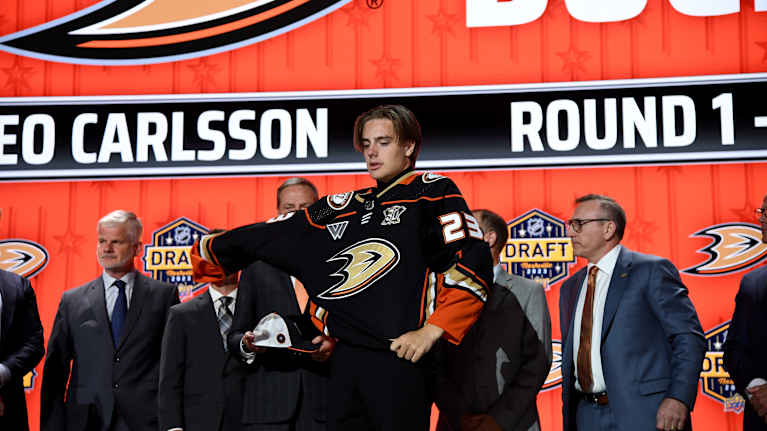 Leo Carlsson sovittaa päälleen Anaheim Ducksin pelipaitaa NHL:n varaustilaisuudessa.